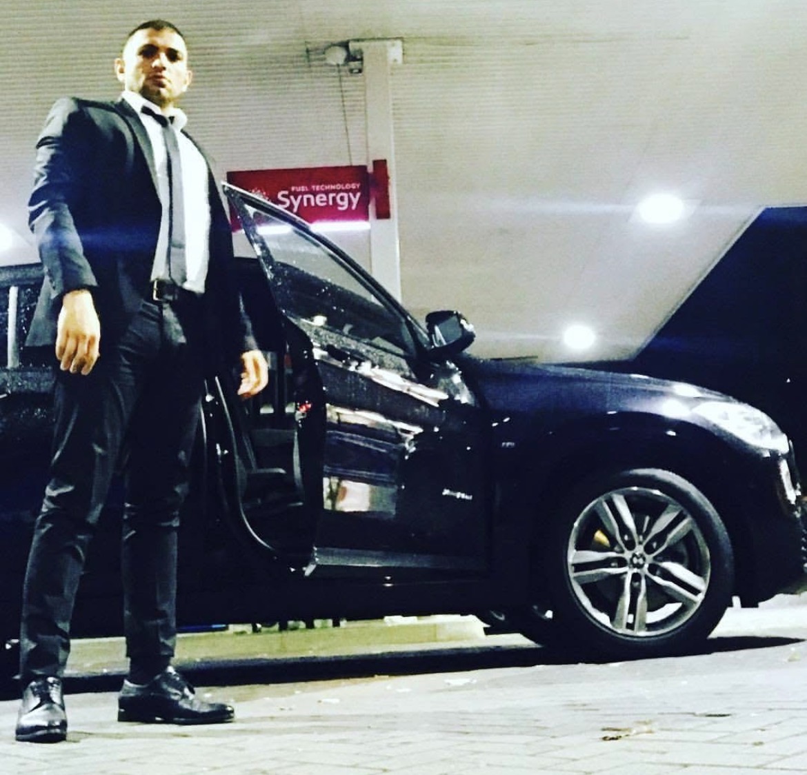 Bank Oliday in tailored suit beside BMW at Shell station